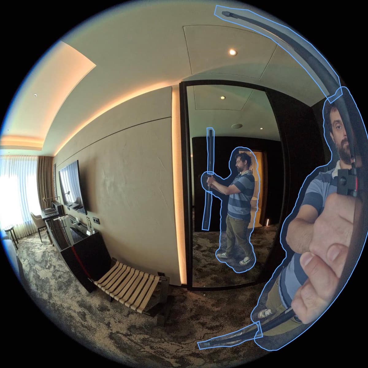 A raw fisheye frame of the hotel room. Blue outlines mark the automatic masks: the person holding the camera, the same person reflected in a mirror, and the camera stick.